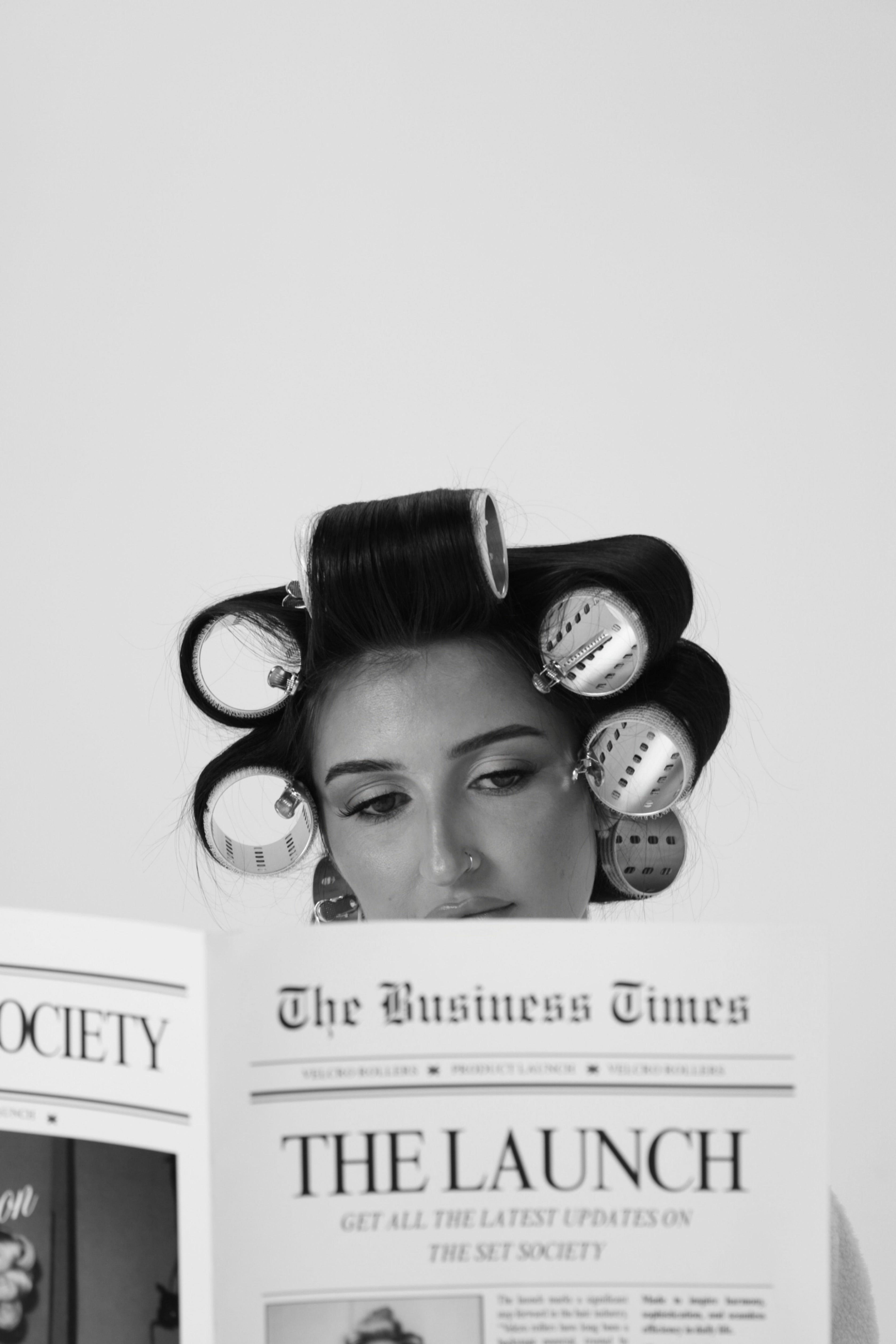 Person with hair in rollers reading a newspaper titled 'The Business Times'.