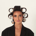 A woman with her hair styled in white large eight rollers wearing a black blazer, photographed against a plain white background.